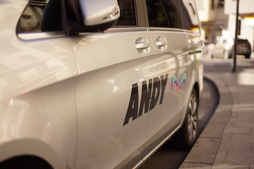 Zilverkleurige ANDY-personenbus op een stadstraat, logo scherp op de deur